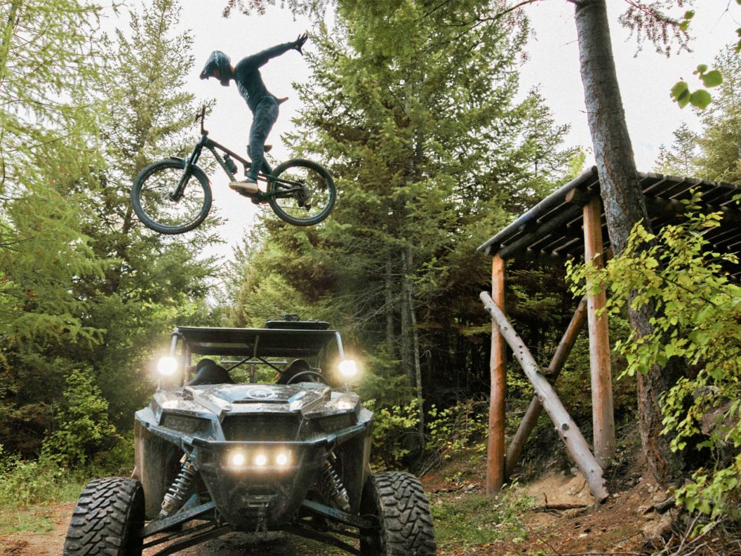 A bike rider spreads their arms and soars over a 4x4 vehicle.